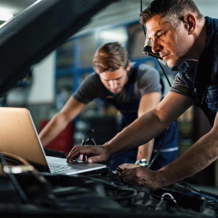 Auto mechanic using laptop while working on car diagnostic with his coworker.