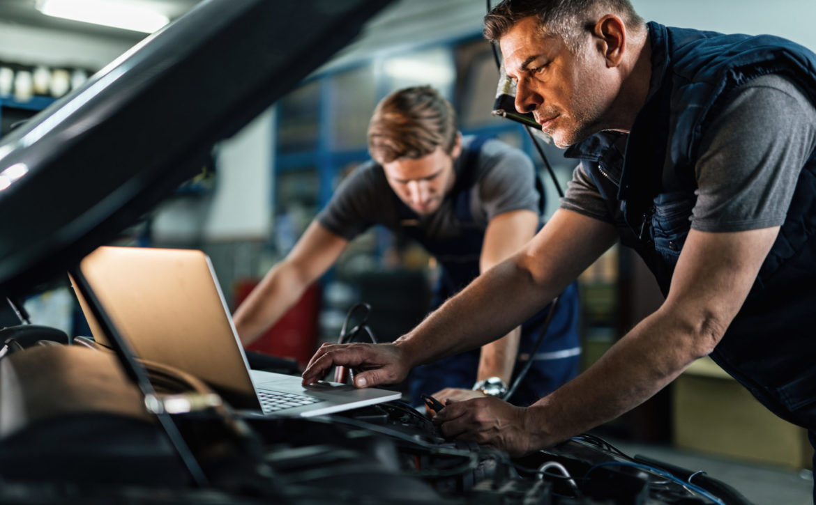Auto mechanic using laptop while working on car diagnostic with his coworker.
